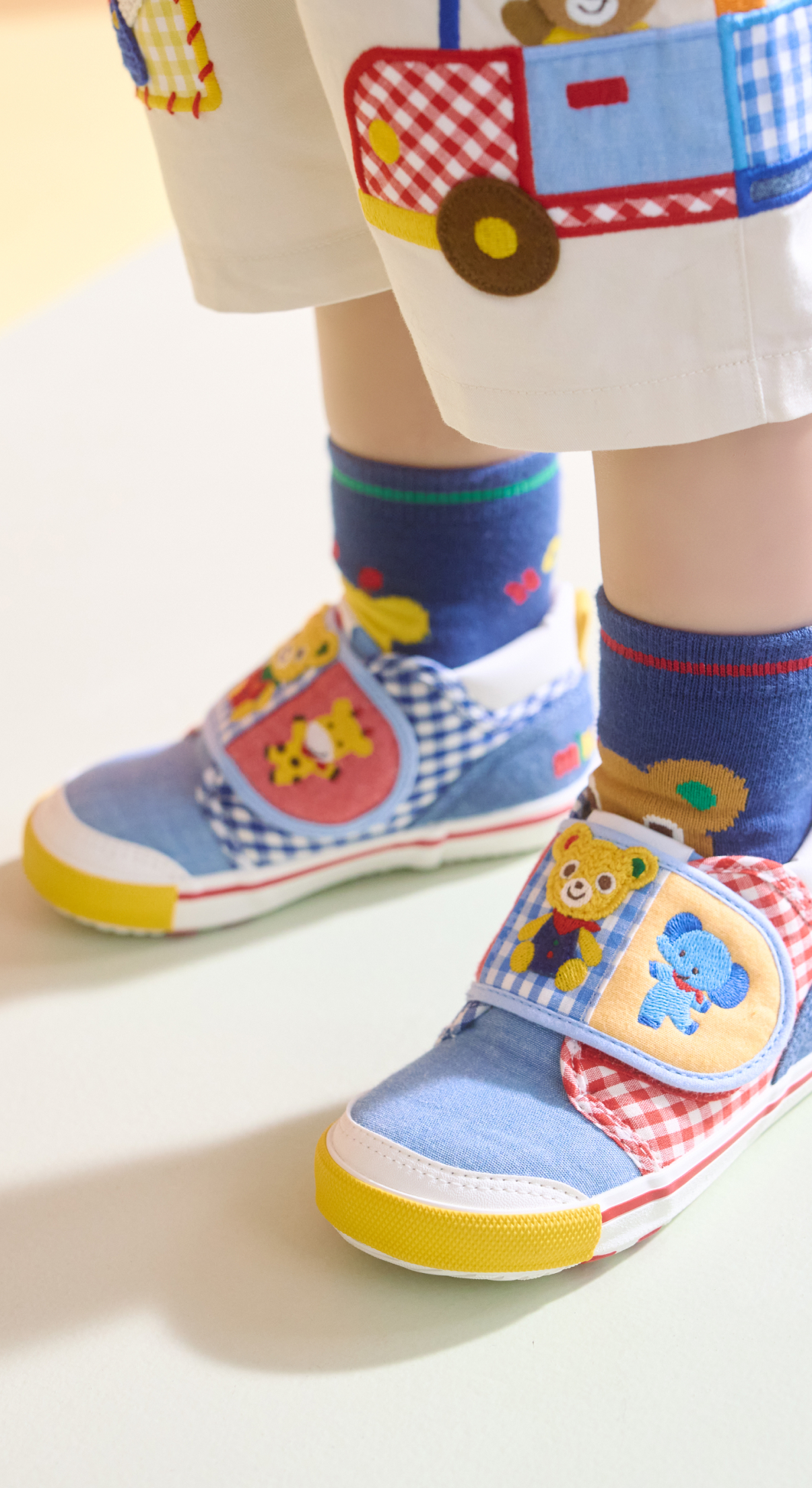 青いトレーナーを着て元気にポーズをとる、笑顔の子どもが白い壁の前に立っている